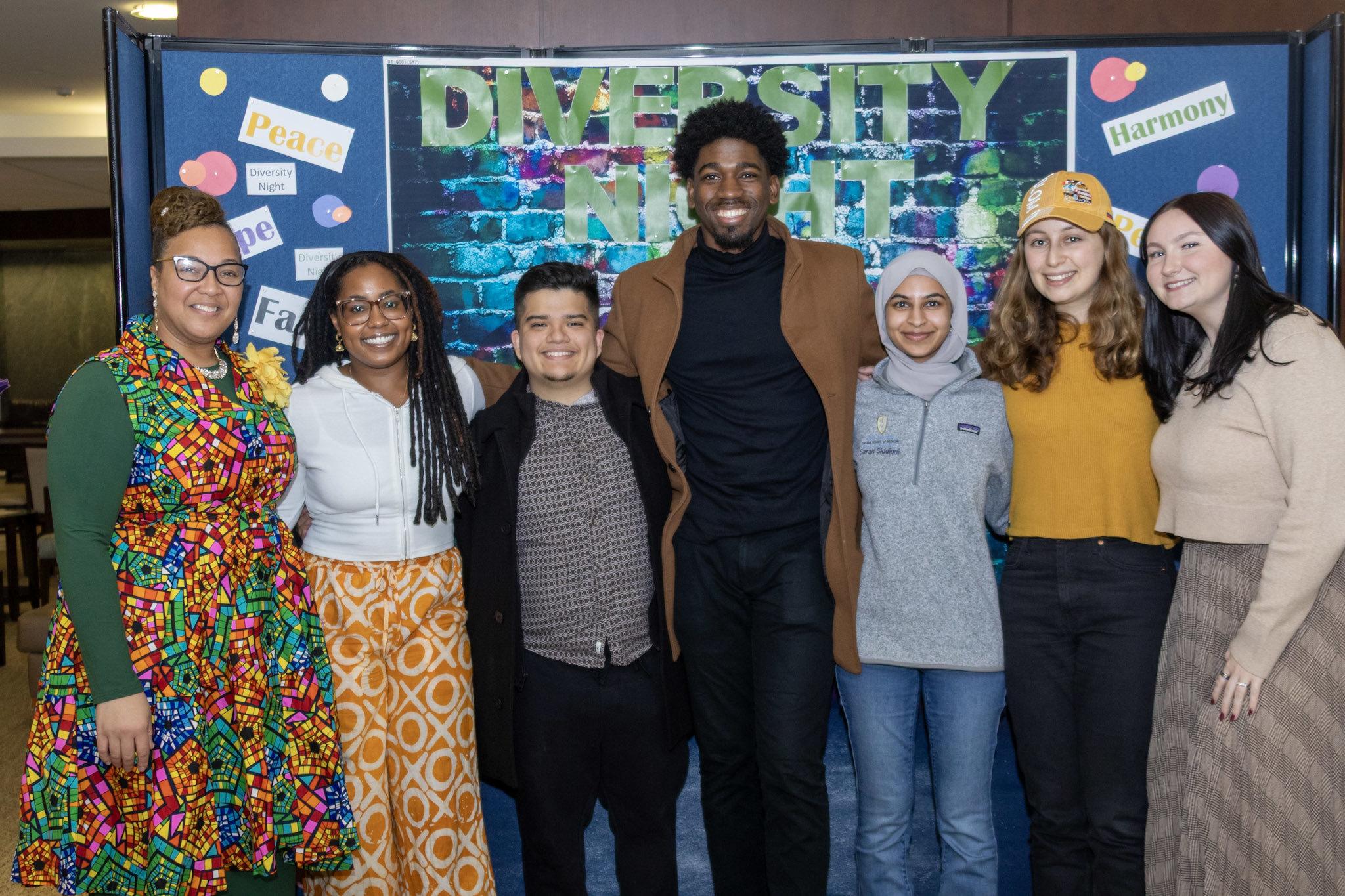 Group of students and staff posing in front of poster