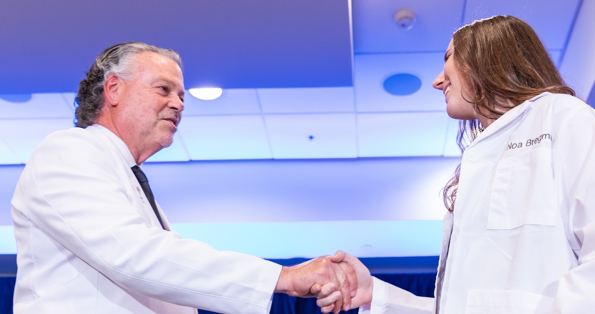 Dean wearing white coat shaking hands with student in white coat