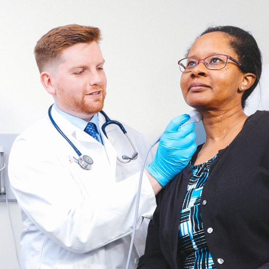 A healthcare professional in a white coat and blue gloves performs an ultrasound procedure on a patients neck in a medical office.