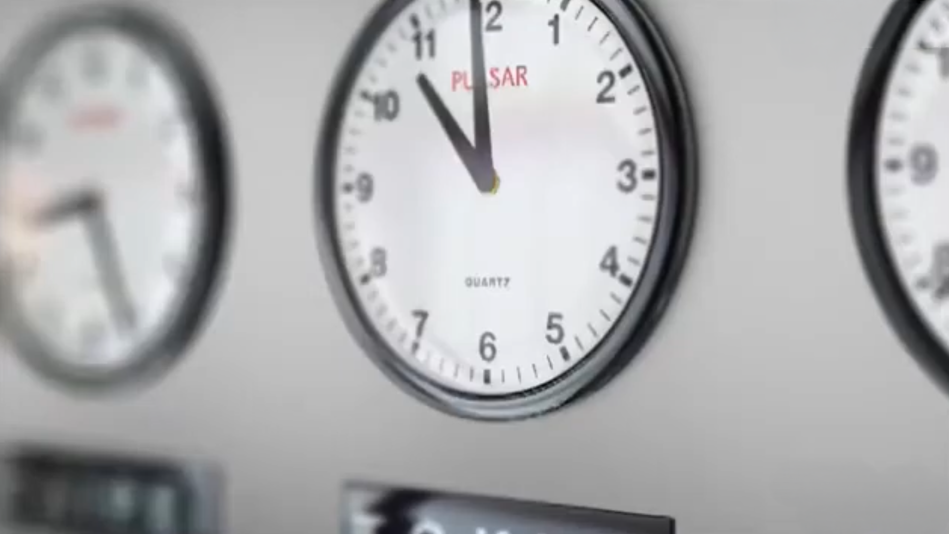 A close-up of three wall clocks, with the center clock showing the time as 11:55. The clocks are mounted on a light-colored wall, and the brand Pulsar is visible on the center clocks face.