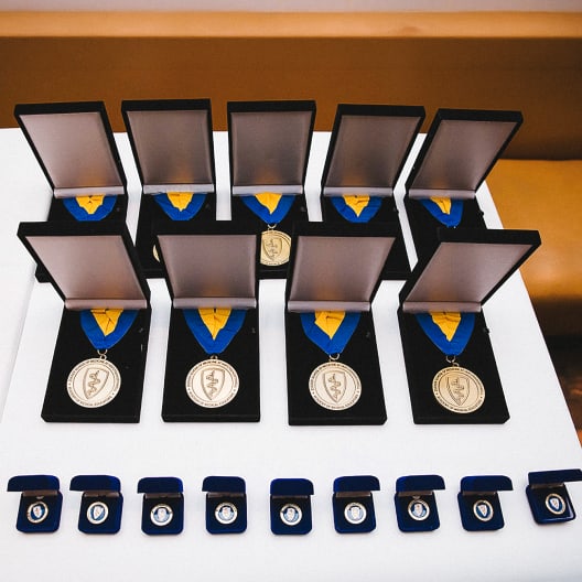 A set of gold medals in open display cases and several smaller pins in blue boxes are neatly arranged on a white table, ready for an award ceremony.